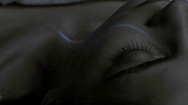 A young woman sleeps alone in a minimal bedroom. Pre-dawn light — not quite darkness, not quite…