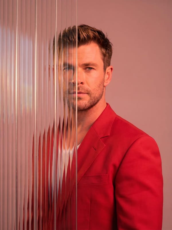 A striking editorial portrait photograph of a person wearing a red blazer, shot against a soft…