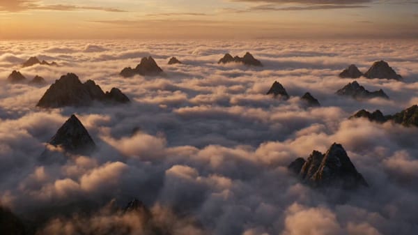 A hyper realistic humpback whale breaches through a sea of clouds above a mountain range, trail…