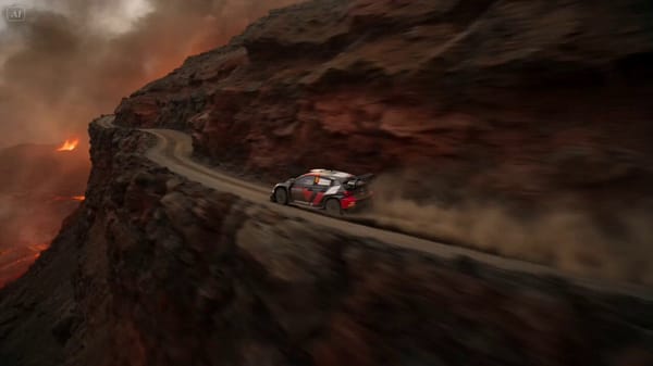 A rally driver speeds along a volcanic cliff road as lava erupts from the mountainside. At the…