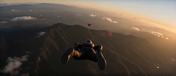 Shot 1 athletic male skydiver in a black tactical wingsuit with dark visor helmet diving vertic…