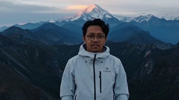 Single shot, static camera framing a wide cinematic composition on a mountain summit at dawn, i…