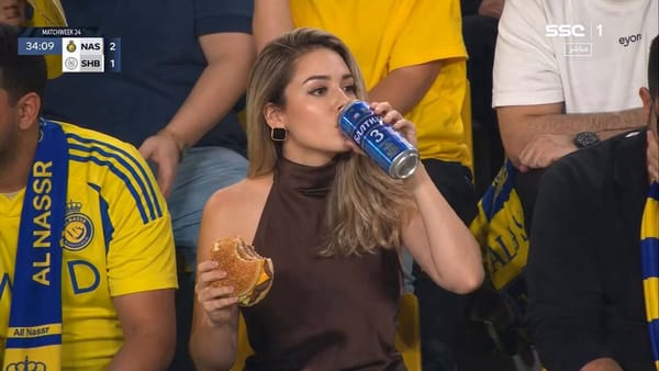 Ultra-realistic sports broadcast still of a glamorous woman sitting in a packed football stadium cr… prompt example
