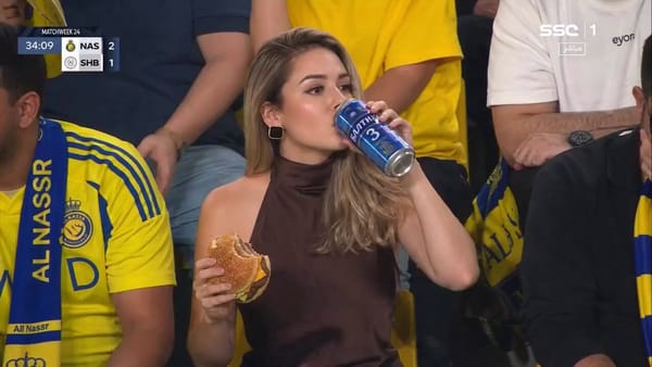 Ultra-realistic sports broadcast still of a glamorous woman sitting in a packed football stadium cr… prompt example