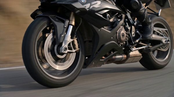 Ultra realistic blonde female rider leaning into a turn on a matte black BMW S1000RR, golden ho…