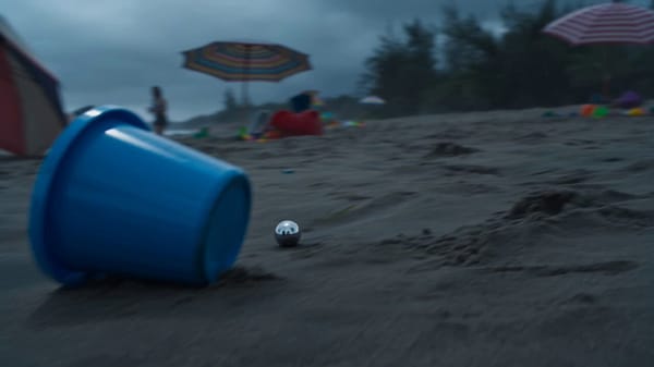 Single continuous cinematic shot on a stormy beach under heavy overcast skies, dark clouds movi…