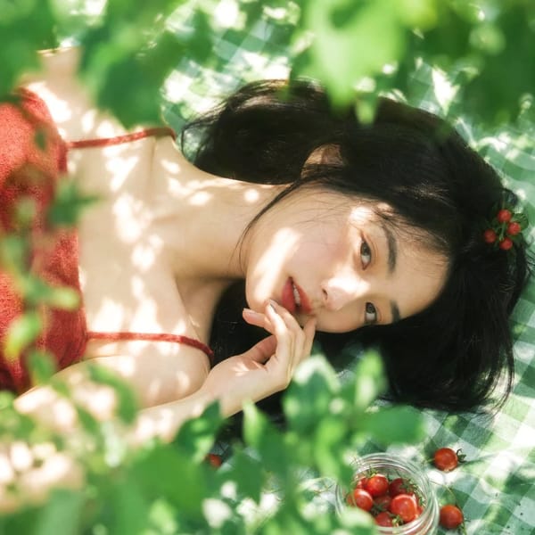 真人摄影，夏日植物系生活方式写真，清透日系胶片感，竖幅 2:3，俯拍近景到面部特写，年轻女性横向躺在绿白格纹野餐布上，脸部位于画面中部偏右下作为主视觉，周围绿植前景占较大比例并形成柔和遮挡，…