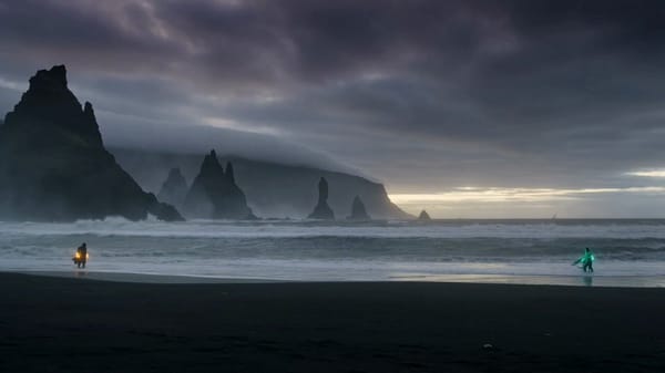 Cinematic dark-fantasy spell duel on a wild storm-lit beach at dusk — vast crashing surf, black…