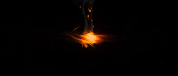Extreme macro on a single ember crawling along a frayed cord against pure black. Frame opens bl…