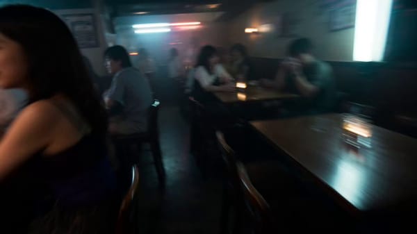快速手持镜头在东京市中心一家热闹拥挤的酒吧舞厅穿梭，夜间（晚上11点），1990年。 镜头在桌椅间移动，捕捉女人们在吧台喝酒，场边走道上三个男女在扭动跳舞、一对情人在做猜拳游戏、三个女人在聊天相互欣… prompt example