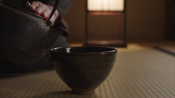 SCENE: Tatami room at night, 16:9. Locked close-up on an adult woman's hands, thirties, pouring…