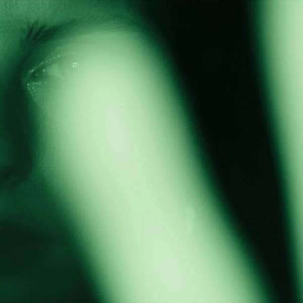 Create an exactly 9 second 1:1 video. Dark feminine young woman in near total darkness, filmed…