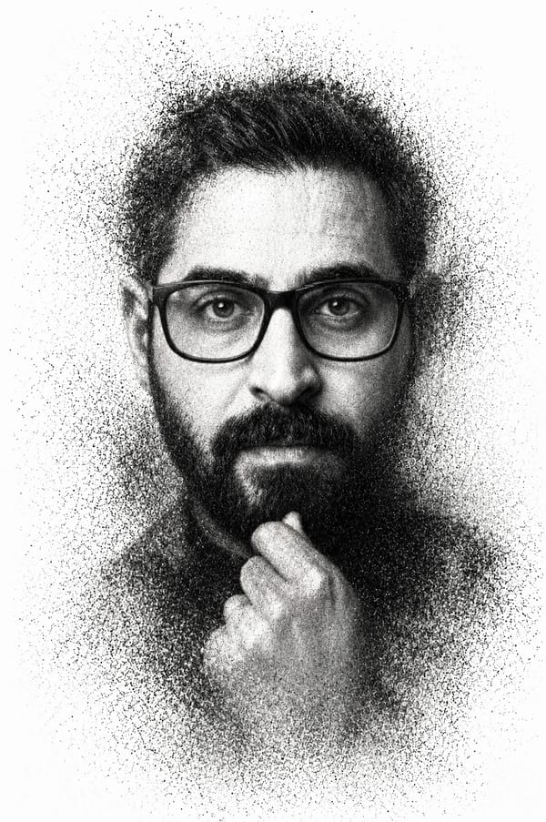 A high-contrast monochrome portrait depicts a man with a groomed beard and thick-rimmed glasses…