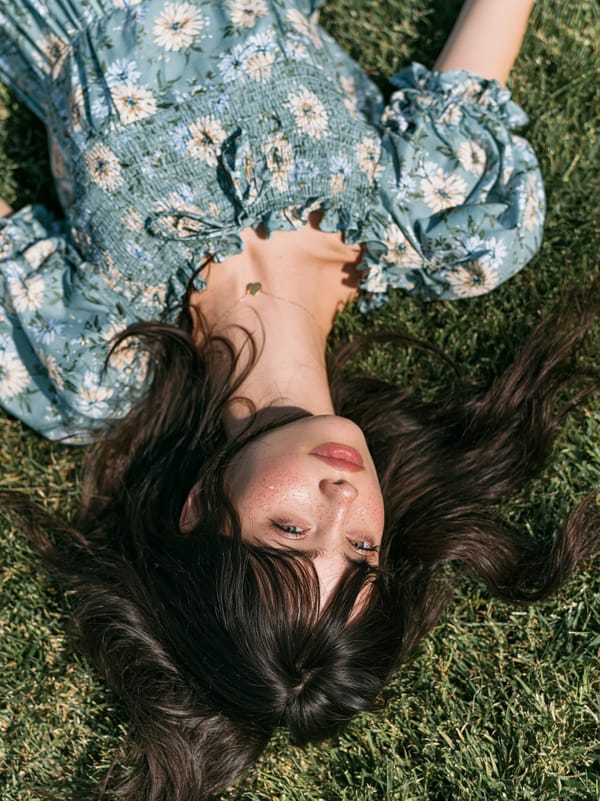 top angle shot of a pretty woman lying on a manicured lawn. woman's is splayed around her, face…